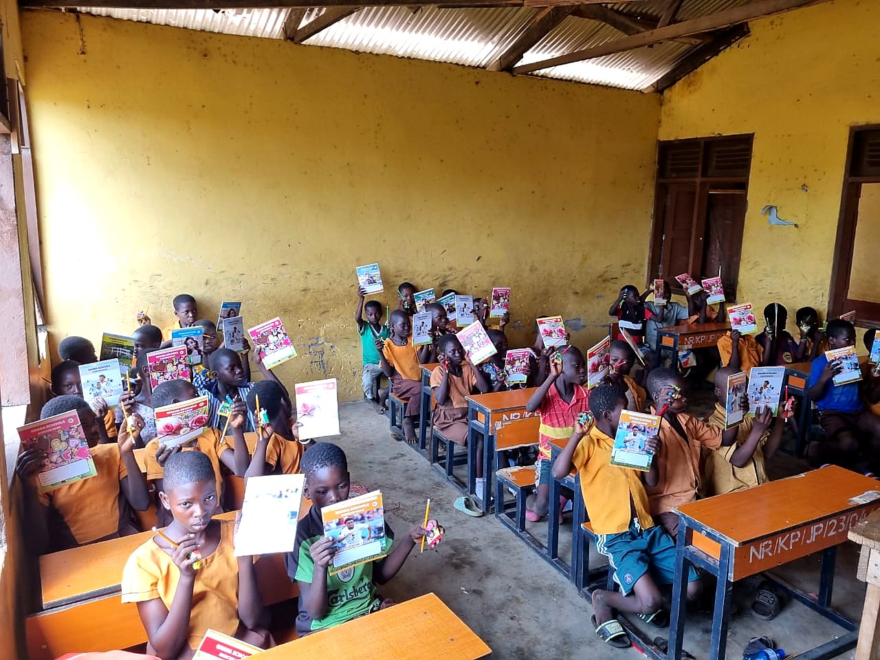 Students in a classroom raising donated books and pencils