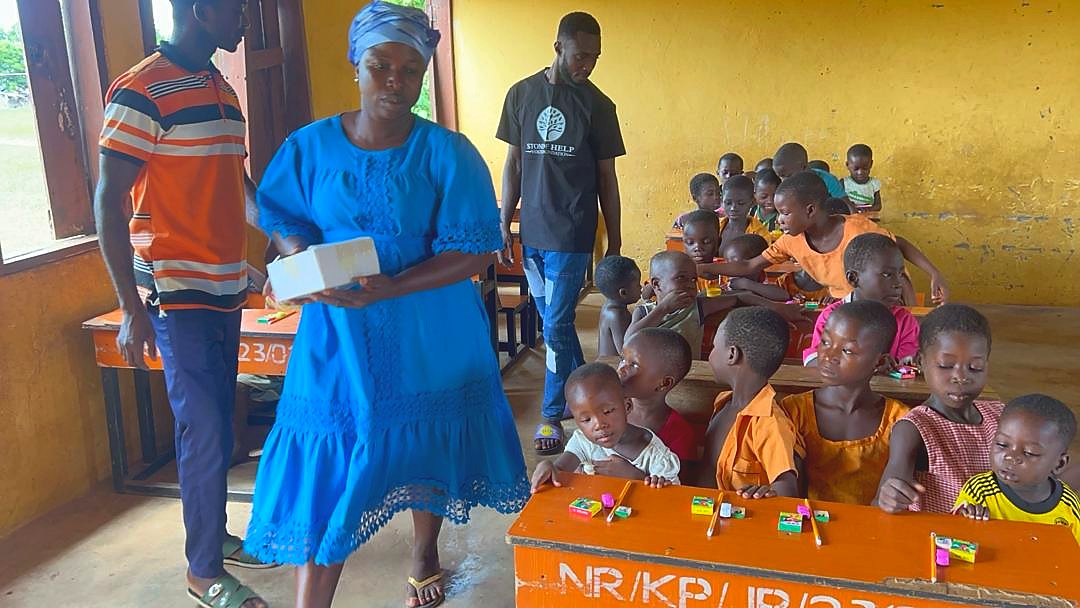 Children seated in a classroom as school supplies are distributed