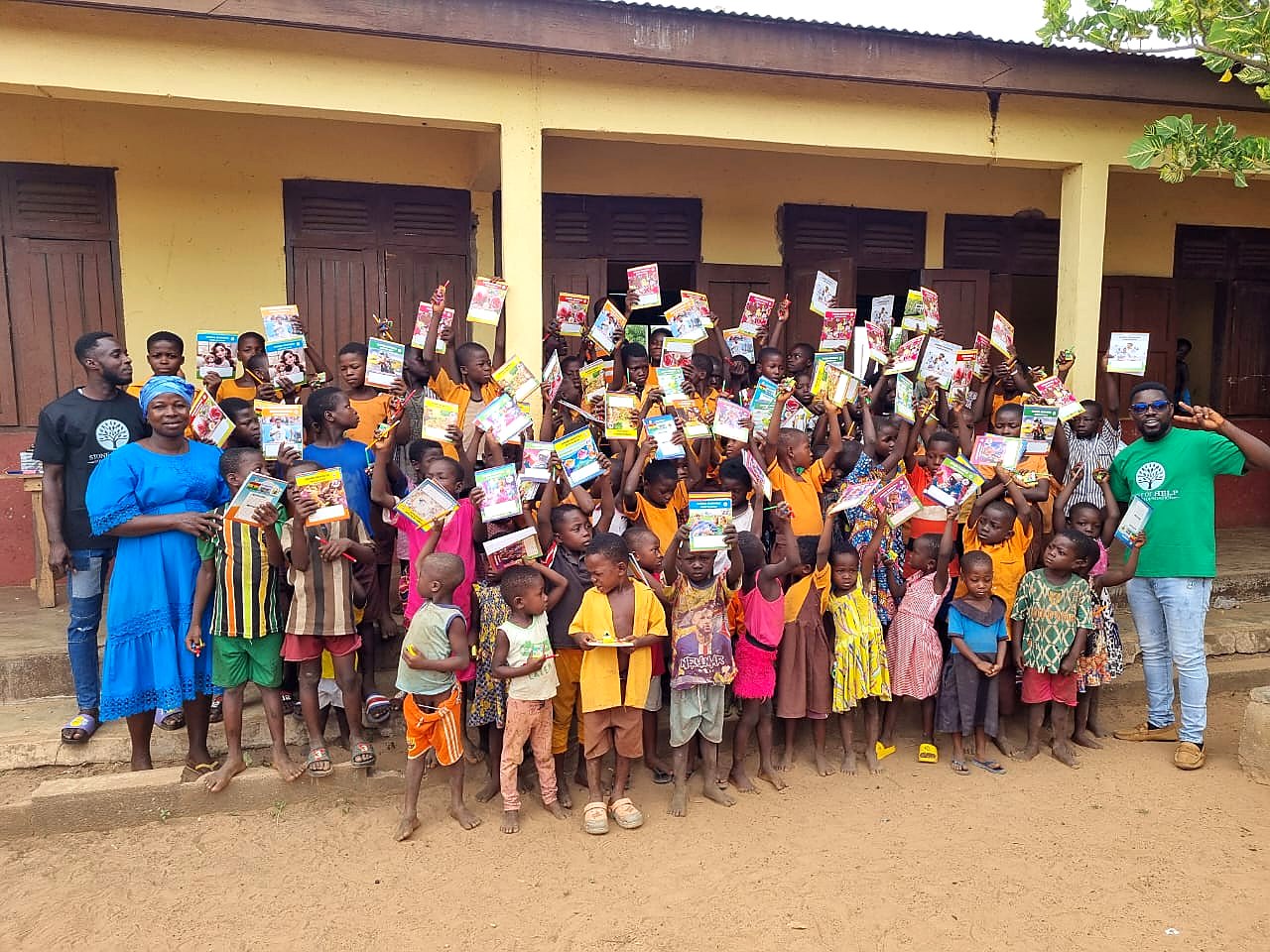 Large group of children holding donated school supplies outside a school building