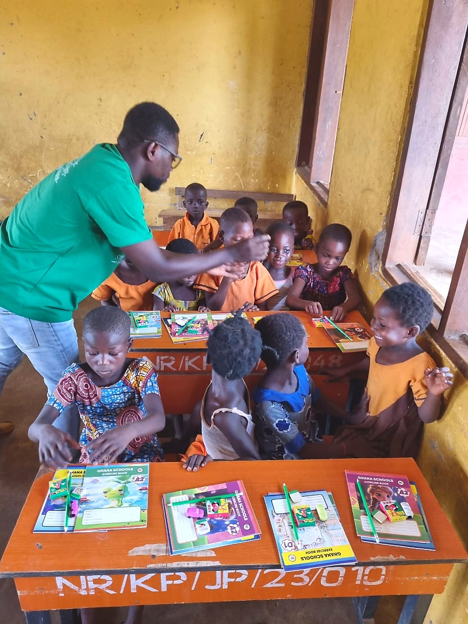 A volunteer encouraging students seated with new exercise books and pencils